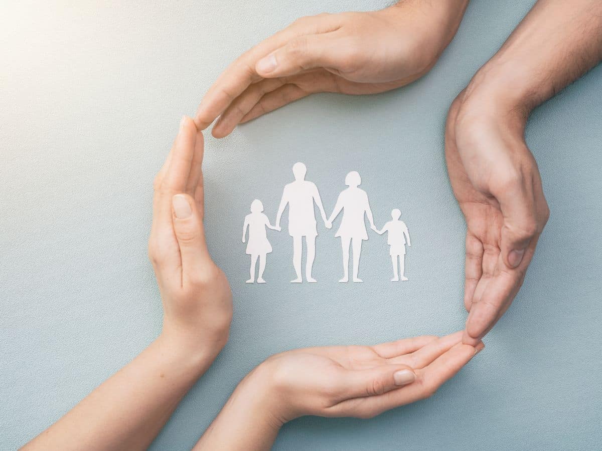 deux paires de mains entourent sur une table les silhouettes en papier d'une famille homme femme et deux enfants