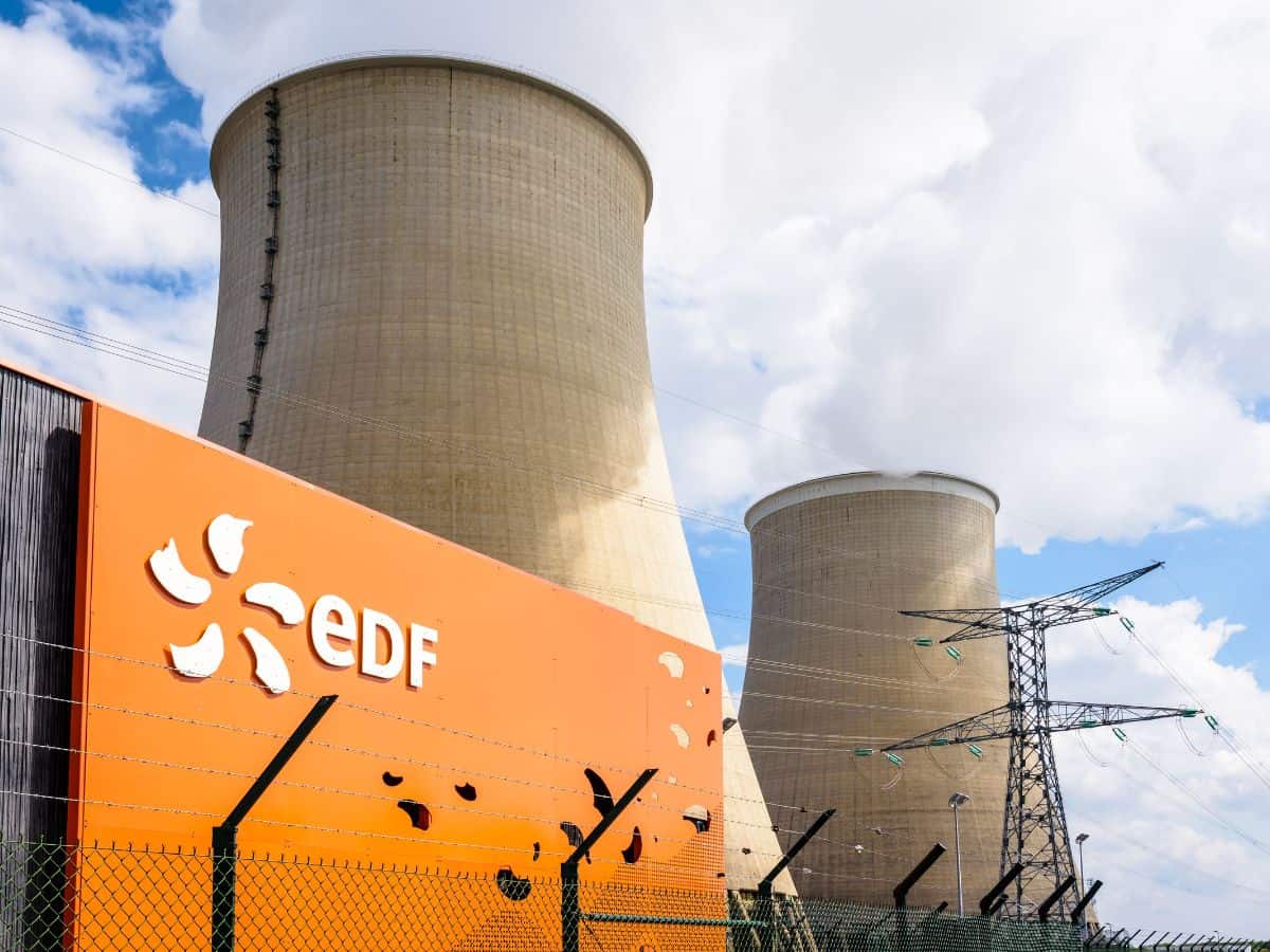 Panneau orange avec logo EDF et ligne électrique au premier plan, deux aéroréfrigérants au second plan avec un ciel nuageux et vapeur d'eau