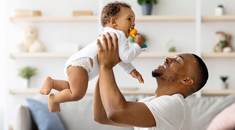 pere porte son fils dans les bras devant lui à la hauteur de son visage