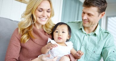 Un couple européen souriant assis sur un canape, la femme a une petite fille asiatique sur les genoux.