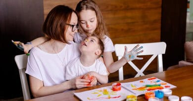 Maman assise à table avec son fils en situation de handicap sur les genoix et sa fille a côté d'elle