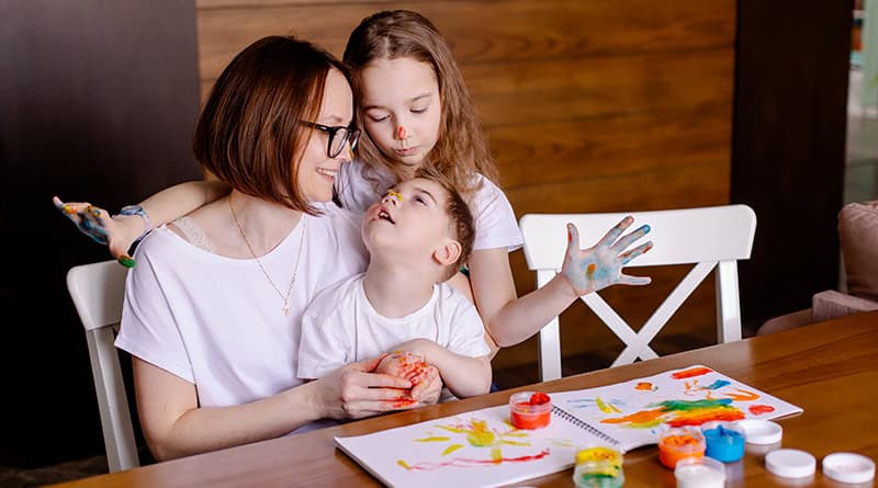 Maman assise à table avec son fils en situation de handicap sur les genoix et sa fille a côté d'elle