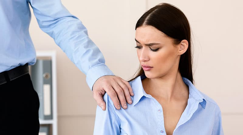 Un homme pose la main sur l'epaule de sa collègue avec insistance