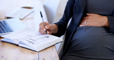 Femme enceinte une main sur le ventre et un stylo à la main ecrit son congé maternité dans son agenda