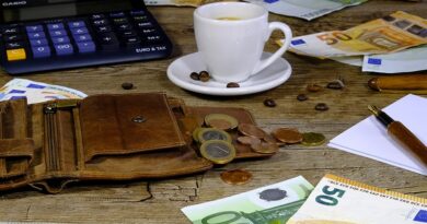 table en bois avec une calculatrice, un vieux portefeuille en cuir ouver, une tasse de café blanche, des billets de 50 et 100 euros avec des pieces.