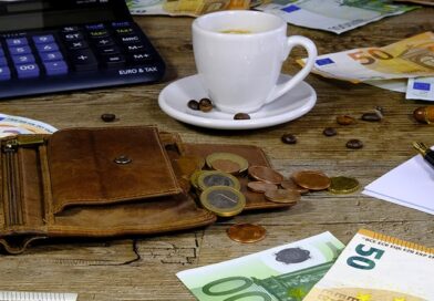 table en bois avec une calculatrice, un vieux portefeuille en cuir ouver, une tasse de café blanche, des billets de 50 et 100 euros avec des pieces.