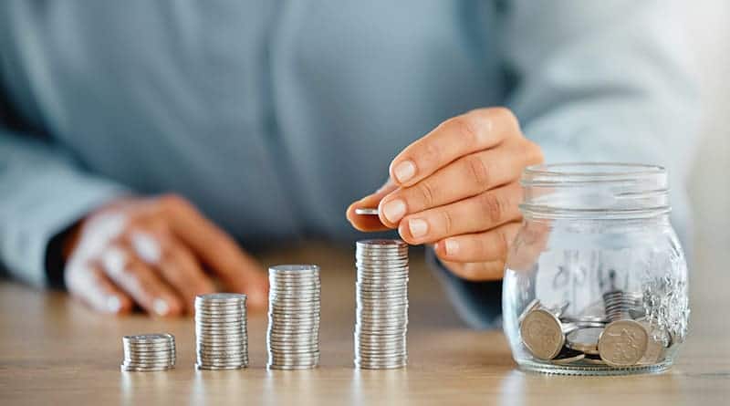 homme fait 4 piles de pieces sur une table avec un bocal plein de pieces