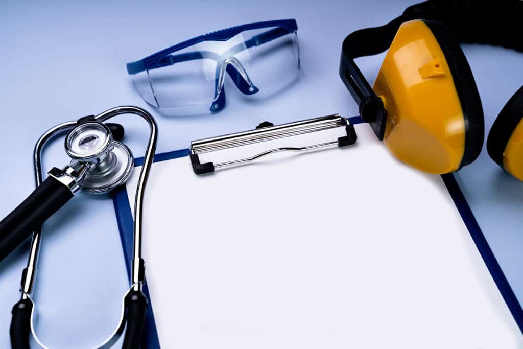 Sur un fond bleu ciel, un stéthoscope, des lunettes de protection, un casque anti bruit et un bloc papier