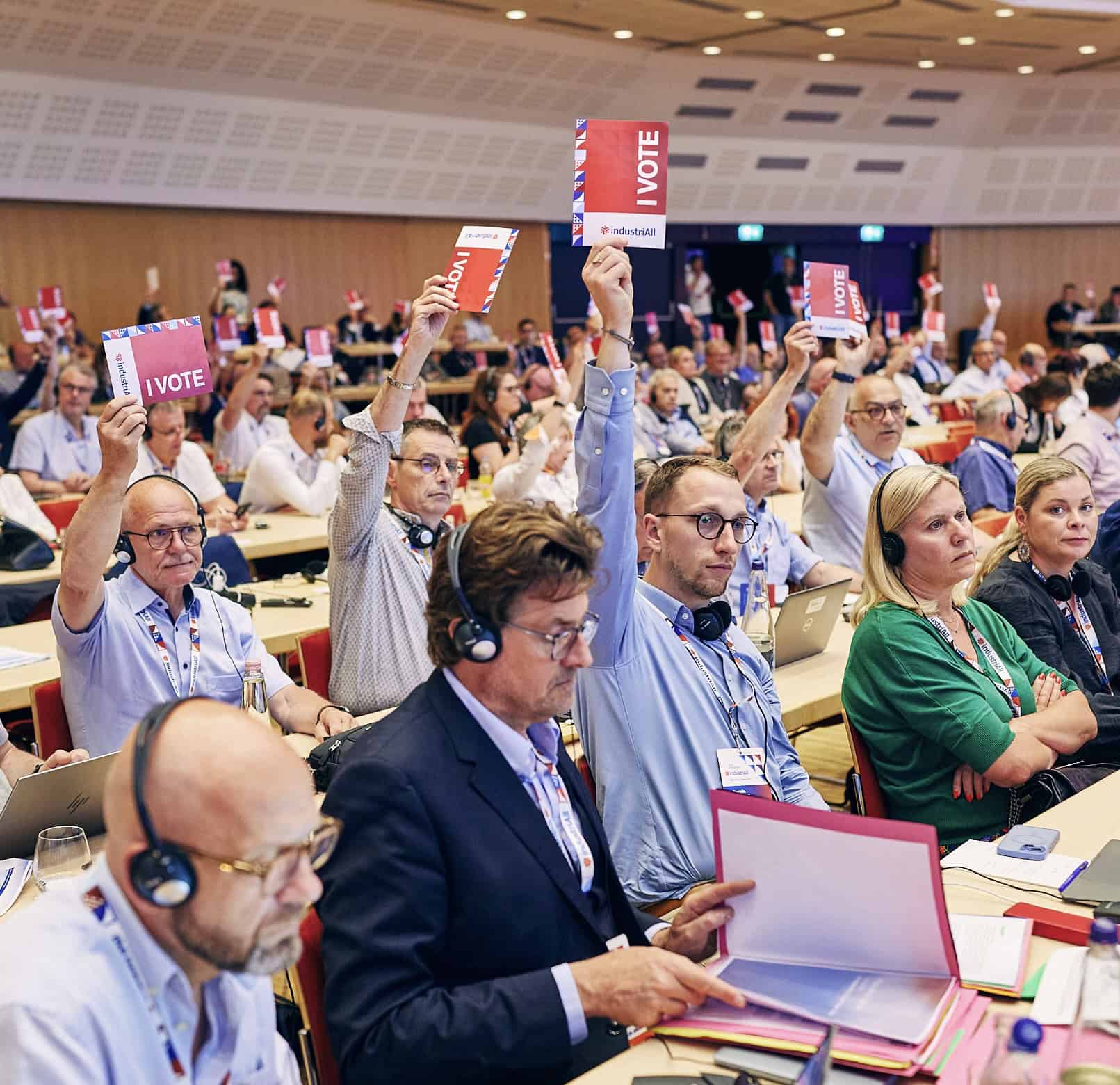 Dans une salle de congrès, des personnes levent les bras pour voter avec un carton de couleur