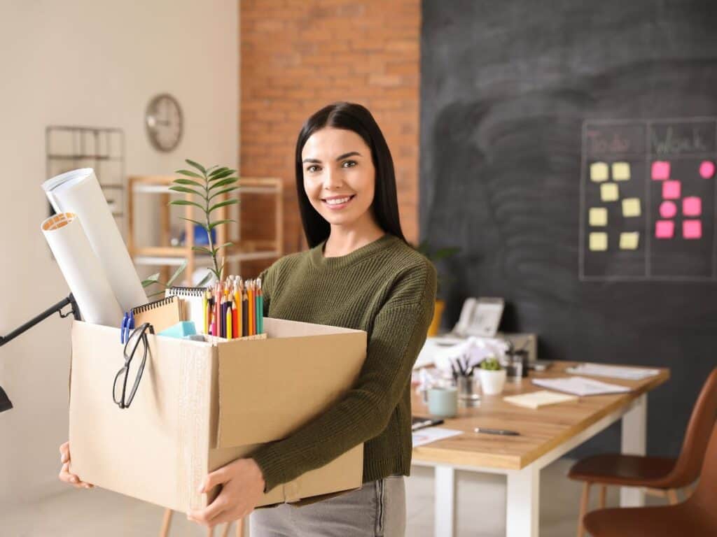 une jeune femme porte un carton avec ses affaires de bureau