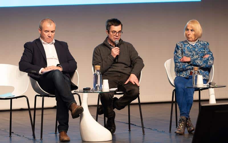 Une femme les bras croisées et deux hommes, assis dans des fauteuils blancs lors du debat sur le projet EPR 2 de Gravelines, l'homme au centre c'est Marc Malhomme, il tient un micro et intervient dans cette réunion "Paroles d'acteurs"